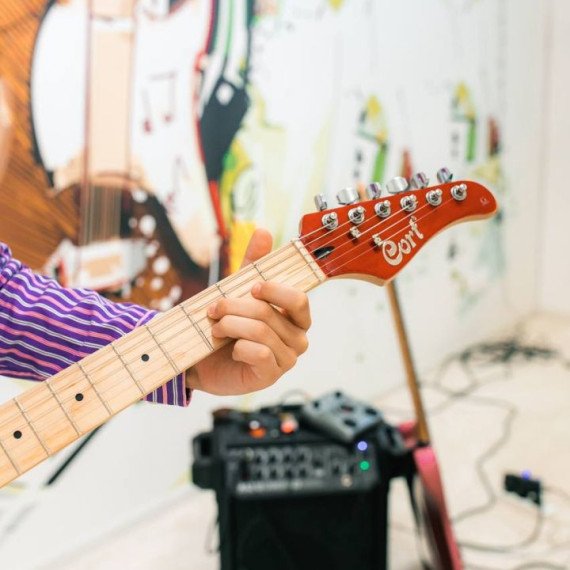 Музыкант играет на гитаре возле электрической установки в современном помещении