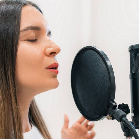 Женщина поёт в студии звукозаписи во время записи трека