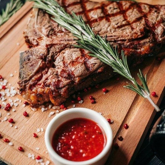 Стейк на деревянной доске с соусом и зеленью рядом на темном фоне. Фото 10