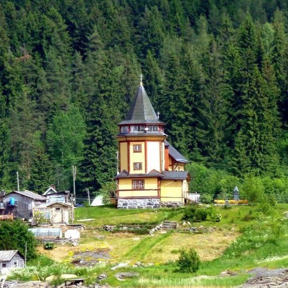 На берегу реки стоит дом с башней среди леса и гор