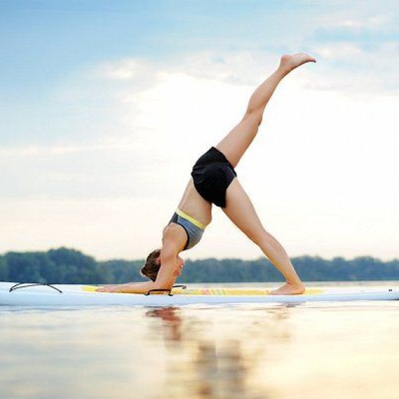 Женщина делает стойку на руках на доске для серфинга на воде в летний день