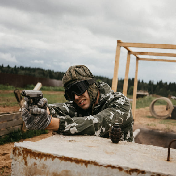 Военнослужащий в камуфляже тренируется с пистолетом на полигоне во время облачной погоды