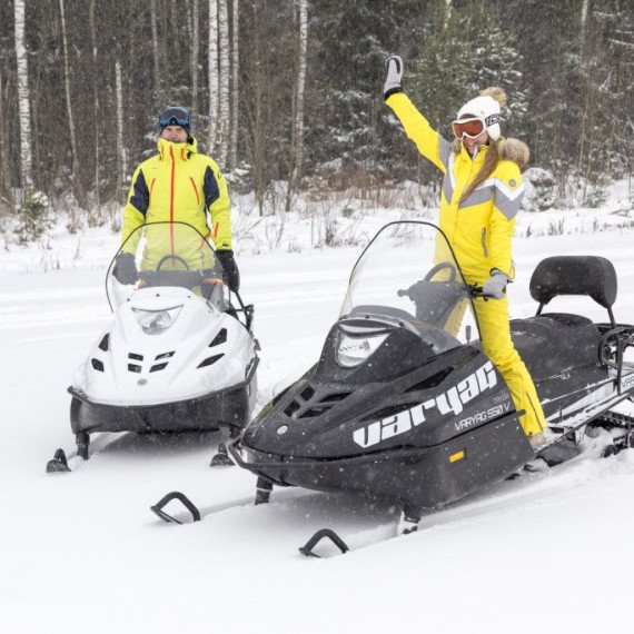 Два человека на снегоходах в зимнем лесу радуются и готовятся к поездке по снегу