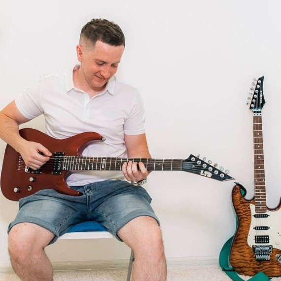 Мужчина играет на электрогитаре в комнате с белыми стенами и двумя гитарами