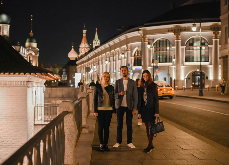 Три человека на набережной Москвы наслаждаются вечерним освещением и атмосферой города поздно ночью