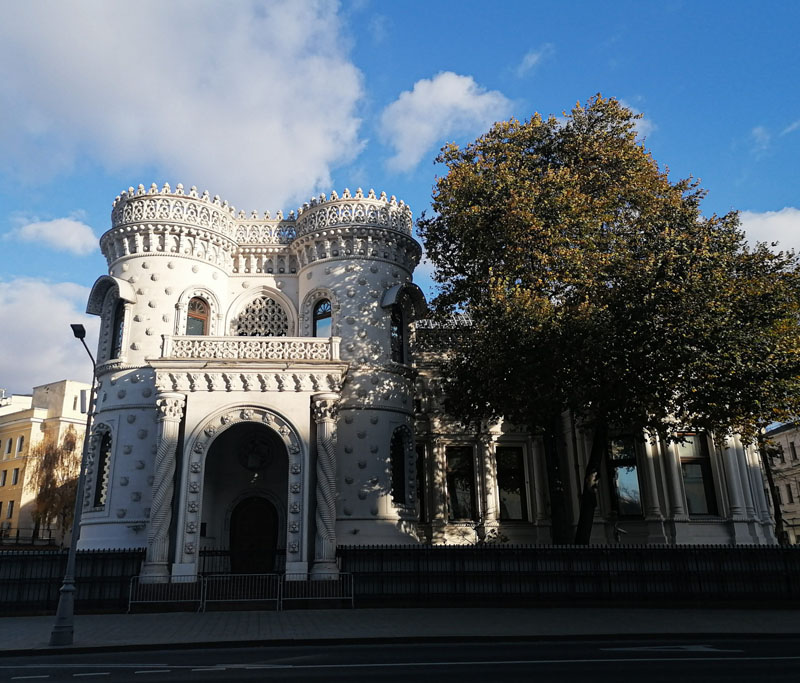 Уникальное здание с белыми башнями и орнаментами в центре города на фоне голубого неба